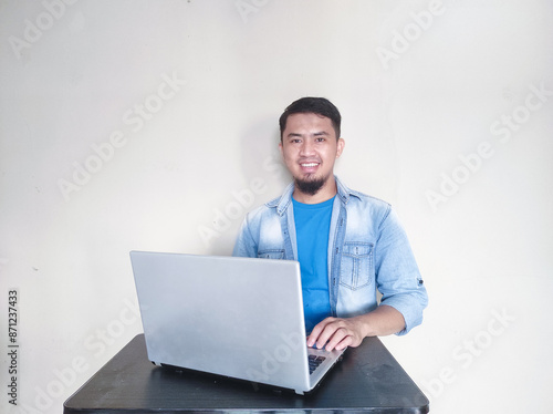 Adult Asian man smiling at camera while using his laptop photo