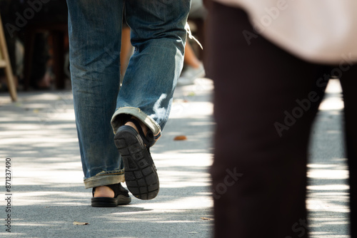 A man in jeans and a black shoe walks down a sidewalk