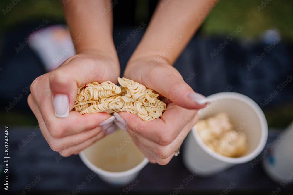 limbazi, Latvia, June 29, 2024 - Close-up of hands breaking instant noodles over paper cups, ready for preparation, outdoor setting with blurred background. limbazi, Latvia, June 29, 2024 - Close-up of hands breaking instant noodles over paper cups, ready for preparation, outdoor setting with blurred background.
