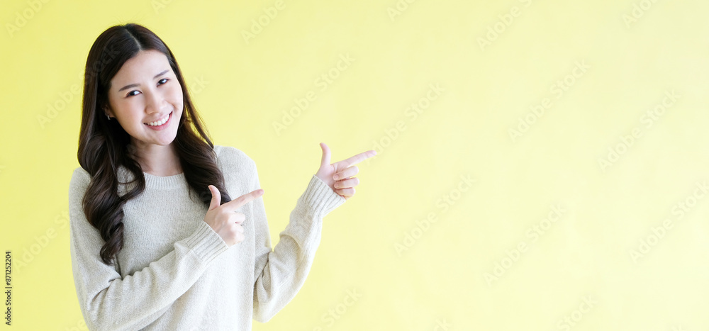 Happy young asian woman pointing hand for presenting product mock up, template while standing over isolated yellow background with copy space Happy young asian woman pointing hand for presenting product mock up, template while standing over isolated yellow background with copy space