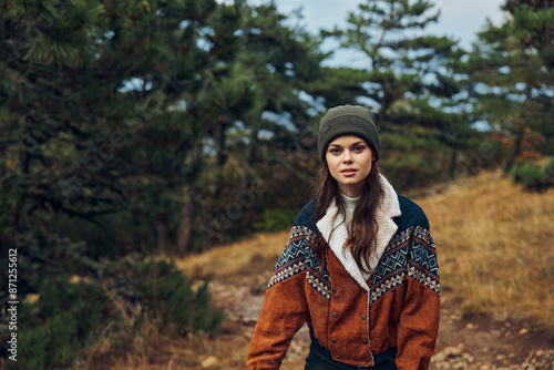 A young woman in a stylish hat and jacket exploring the beauty of nature on a serene forest path