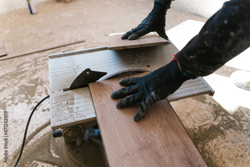 Crop carpenter cutting wooden board in workshop with electric saw