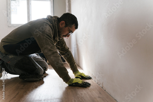 Male worker installing wooden floor in apartment