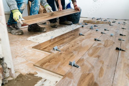 Unrecognizable workmen installing laminate wood flooring in apartment