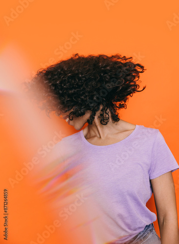 Woman with curly hair in lilac top against vibrant orange background