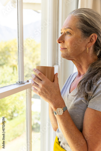 Free Download Holding cup, mature woman looking out window, enjoying peaceful moment - GFXLoad