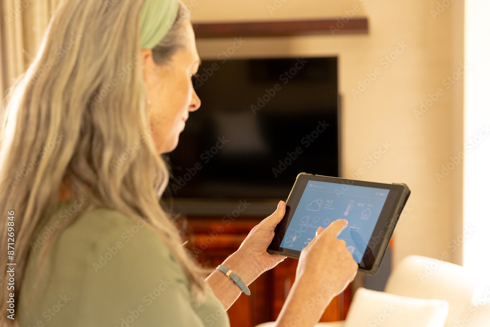 Using tablet, mature woman controlling smart home devices in living room Using tablet, mature woman controlling smart home devices in living room