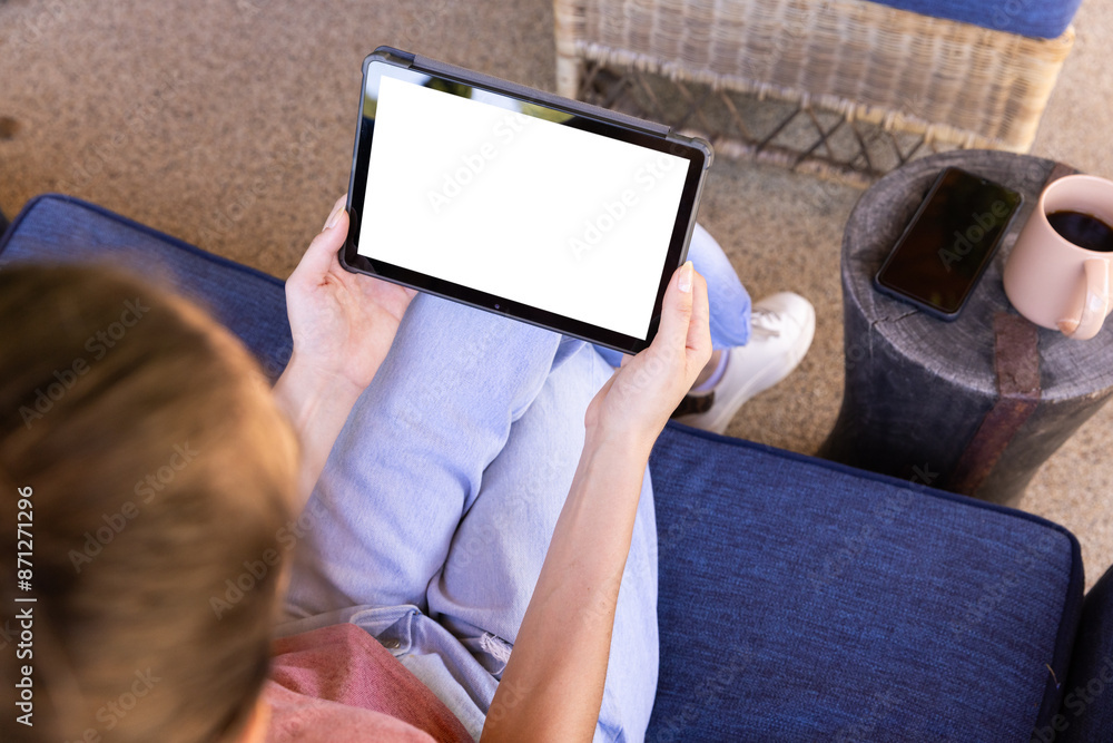 Naklejka premium Using tablet while sitting on couch, young woman relaxing at home, copy space