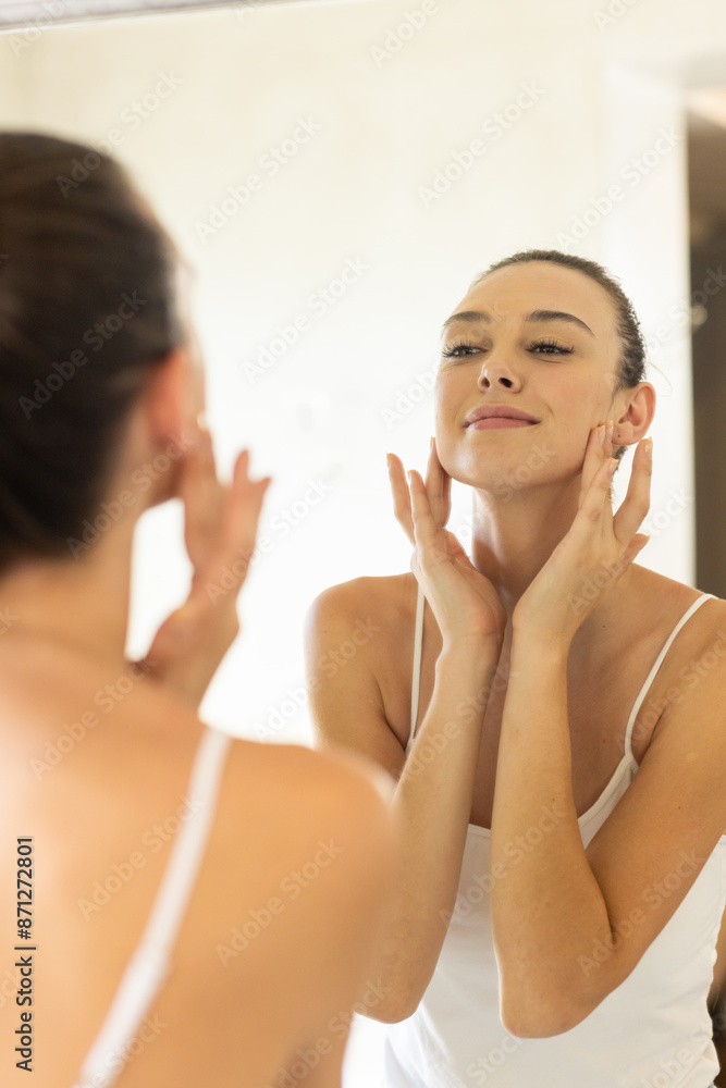 Applying skincare, young woman looking in mirror and touching face at home Applying skincare, young woman looking in mirror and touching face at home