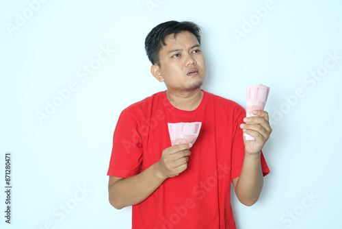 Young Asian man thinking about something when counting his paper money. Wearing red t-shirt