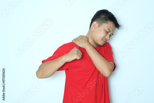 Young Asian man touching his right shoulder with pain expression. Wearing red t-shirt photo
