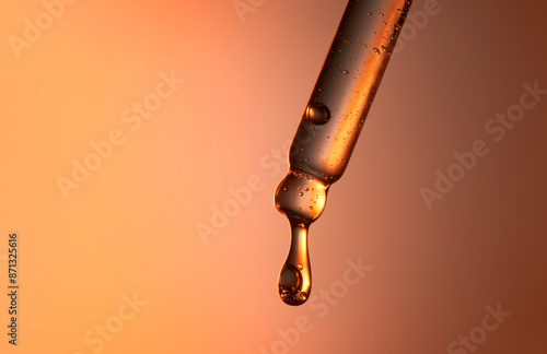 Clear glass pipette with a drop of cosmetic product falling down. 