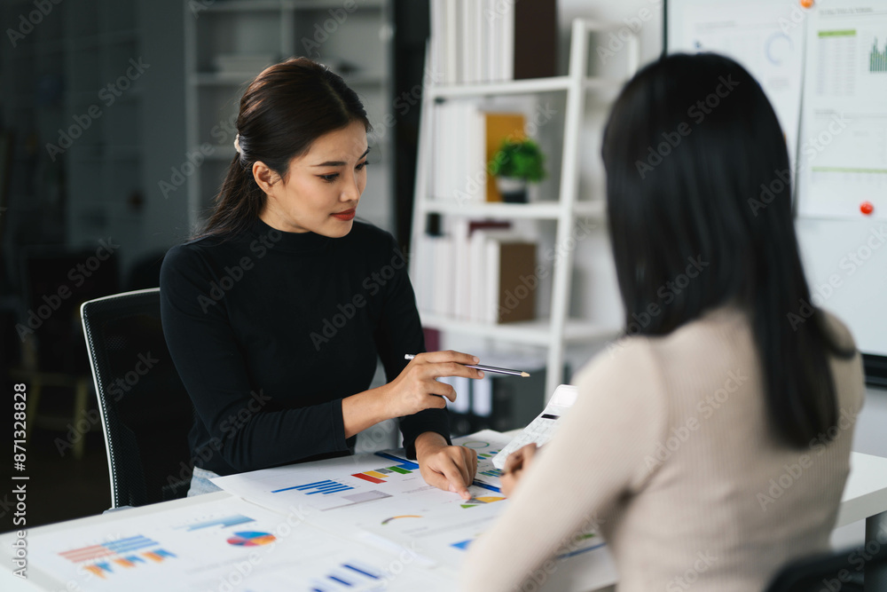 Fototapeta premium Two Businesswomen Analyzing Financial Charts in Modern Office Setting