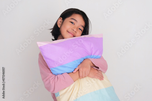 Little girl smiling at the camera while hugging a sleeping pillow photo