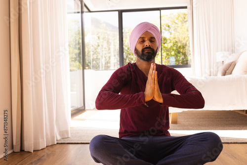 Meditating at home, man in turban sitting cross-legged with hands together, copy space