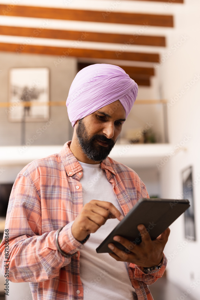 Using tablet, man in turban browsing internet in modern home setting Using tablet, man in turban browsing internet in modern home setting