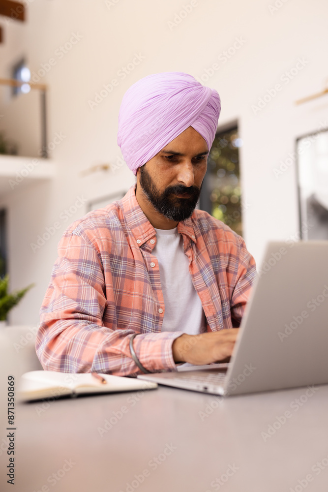 Using laptop, man in turban working from home with notepad on table Using laptop, man in turban working from home with notepad on table