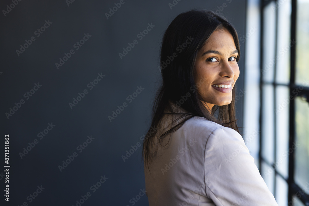 Smiling businesswoman standing by window, looking confident in office setting, copy space Smiling businesswoman standing by window, looking confident in office setting, copy space