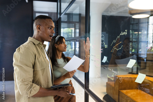 Discussing business strategy, colleagues analyzing charts and graphs on glass wall photo