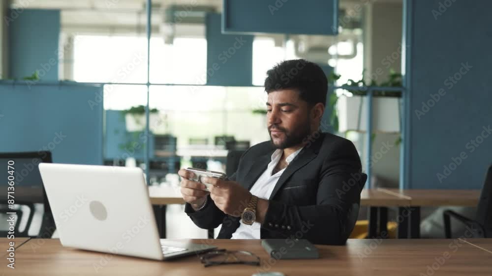 portrait of a handsome, stylish young man of Arab appearance sitting in a modern office of a business center, playing a game on his smartphone and celebrating his victory portrait of a handsome, stylish young man of Arab appearance sitting in a modern office of a business center, playing a game on his smartphone and celebrating his victory