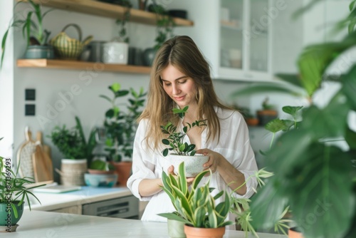 A woman tends to houseplants in a bright, plant-filled kitchen. She holds a potted plant, surrounded by greenery on shelves and countertops. © Kishore Newton