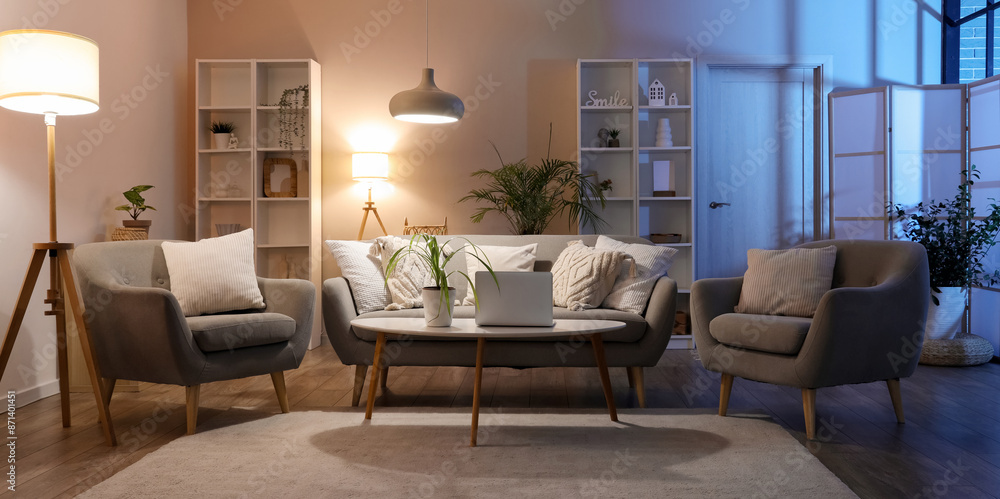 Fototapeta premium Interior of cozy living room with sofa, table, armchairs and glowing lamps in evening