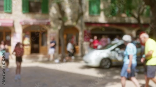 Wallpaper Mural Blurred people walking in an outdoor plaza in mallorca with a stone building and green shutters in the background Torontodigital.ca