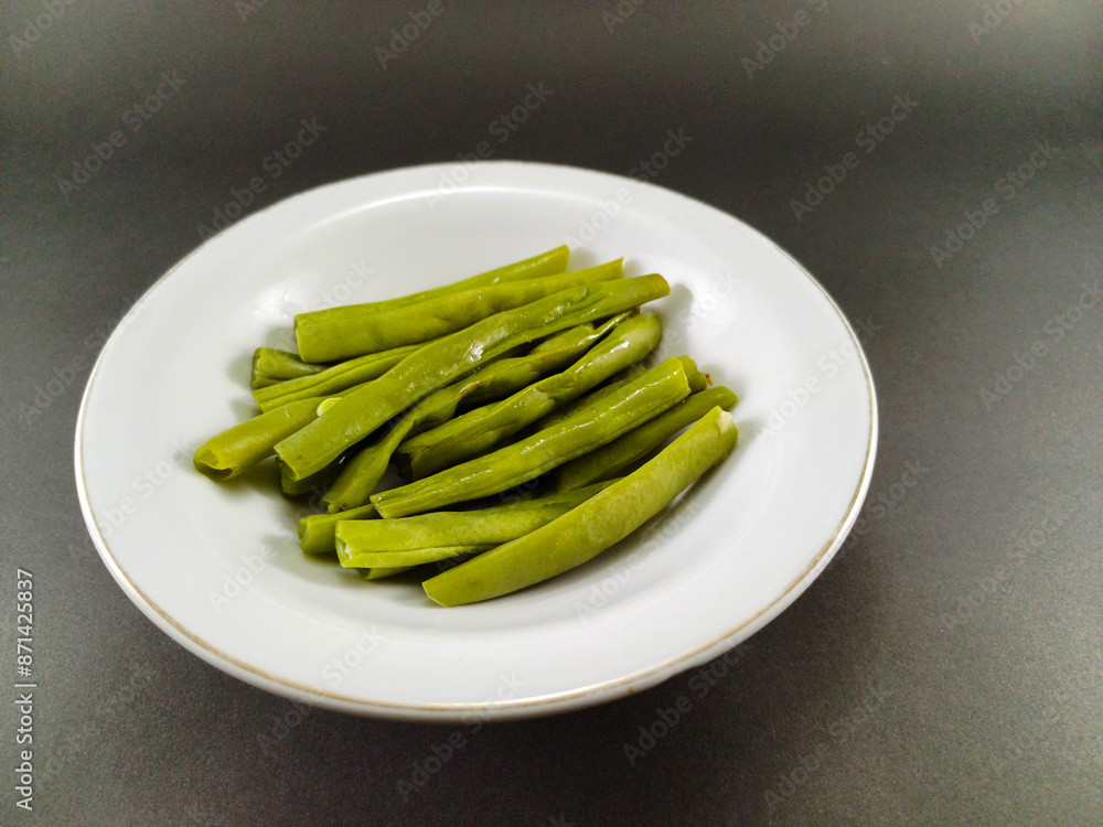 Chopped green beans neatly placed in a white bowl, set against a contrasting dark grey ash background, creating a visually striking and appetizing presentation Chopped green beans neatly placed in a white bowl, set against a contrasting dark grey ash background, creating a visually striking and appetizing presentation