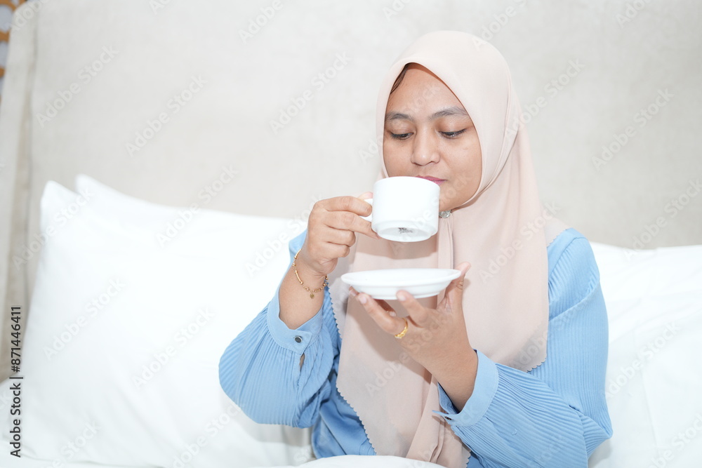 Muslim woman is relaxing while enjoying a cup of tea on the bed Muslim woman is relaxing while enjoying a cup of tea on the bed