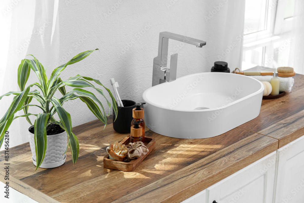Fototapeta premium Chest of drawers with sink, houseplant and bath supplies near white wall in bathroom