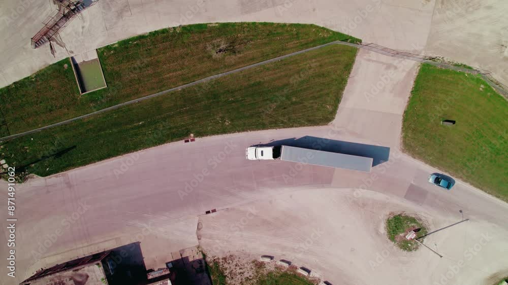 Aerial shot of a dry van truck entering and leaving the frame on a curved road with green patches on either side.