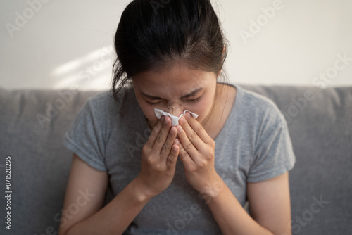 Asian young woman have a fever, flu sore throat, use tissues paper sneezing runny nose, sick, hurt or pain while sitting rest on sofa at home. Health care on virus infective, allergy person