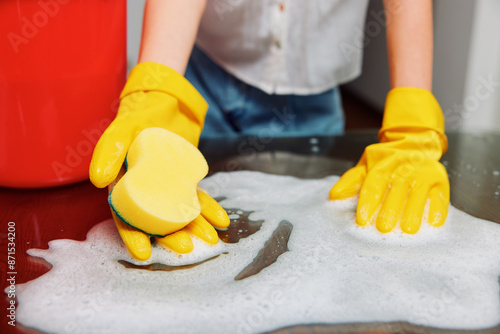 Woman in yellow rubber gloves cleaning a countertop with soap and sponge