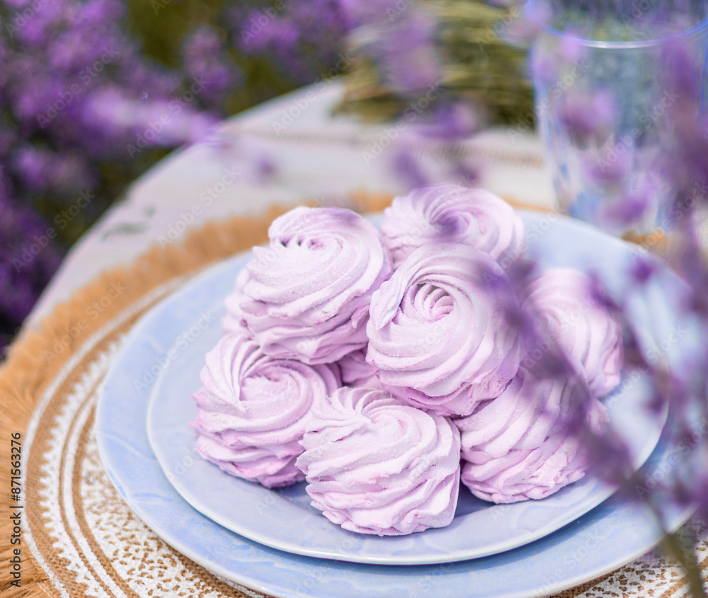 marshmallow on plate on table in lavender field with cup of tea and kettle, tasty homemade zephyr purple color.candles as decor.bee on flowers, summer time. marshmallow on plate on table in lavender field with cup of tea and kettle, tasty homemade zephyr purple color.candles as decor.bee on flowers, summer time.