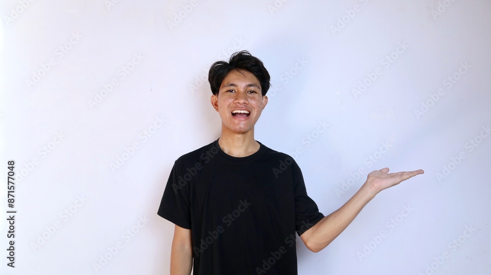 Excited young Asian man wearing black shirt with open palm gesture showing a product, copy space, advertising, marketing Excited young Asian man wearing black shirt with open palm gesture showing a product, copy space, advertising, marketing