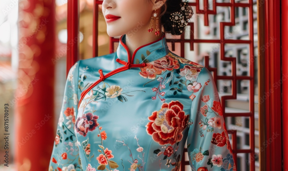 Obraz premium beautiful Chinese woman in embroidered blue cheongsam with red trim, floral pattern with peonies, traditional hairstyle, modern street scene with red metal lattices, close-up in soft light