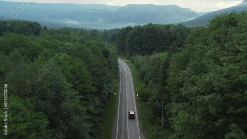 A black SUV drives along the road through a forest belt, mountains are visible in the distance
