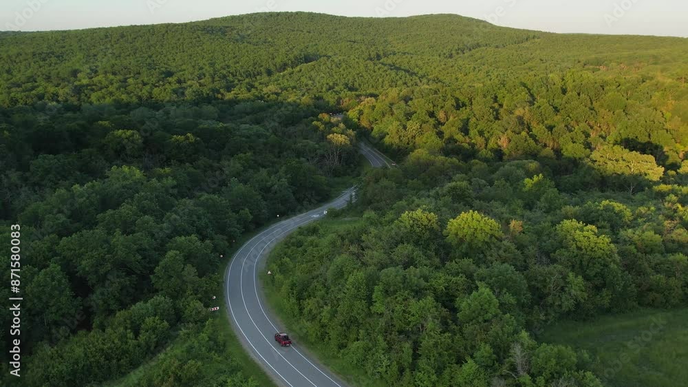 Red car driving along a winding mountain forest road, warm and summer weather Red car driving along a winding mountain forest road, warm and summer weather