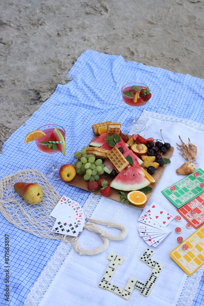 Fototapeta premium summer picnic on the seashore. board games on a picnic blanket. dominoes, lotto and cards. fruits and berries for a snack