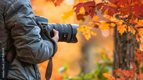 Professional Photographer Holding Camera Against Vibrant Autumn Foliage, Capturing Moments with Elegant and Professional Look in Soft Light, Perfect for Photography Enthusiasts in Commercial Style.