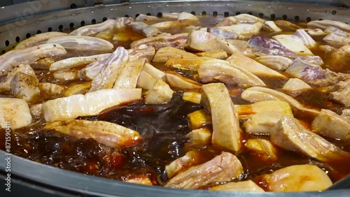 Obraz na plátně Pork ribs are being cooked on an industrial scale in large pans, simmering in a rich broth