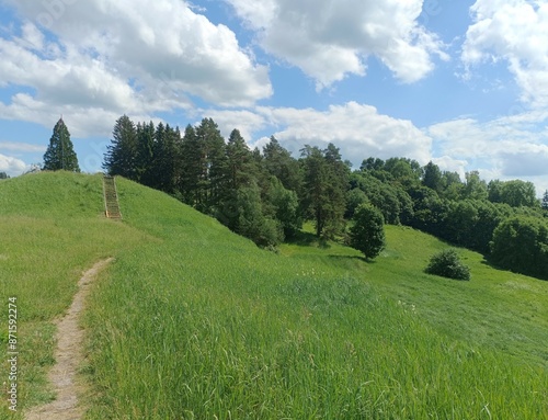 Bubiai hill during sunny day. Small hill. Grass is growing on hill. Staircase leading to the top. Sunny day with white and gray clouds in sky. Nature. Bubiu piliakalnis. photo