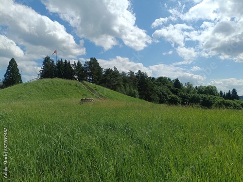 Bubiai hill during sunny day. Small hill. Grass is growing on hill. Staircase leading to the top. Sunny day with white and gray clouds in sky. Nature. Bubiu piliakalnis. photo