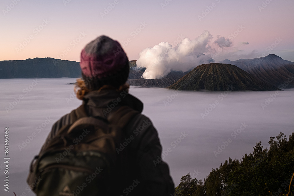 A young girl, a traveler, of European appearance, wearing a knitted hat, admires the stunning view of the Bromo volcano on the island of Java, Indonesia. A young girl, a traveler, of European appearance, wearing a knitted hat, admires the stunning view of the Bromo volcano on the island of Java, Indonesia.