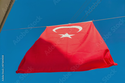 Turkey's red flag with a white crescent moon and a five-pointed star hangs on a rope between houses against a clear blue sky. Symbols of statehood, patriotism, signs, symbolism. photo