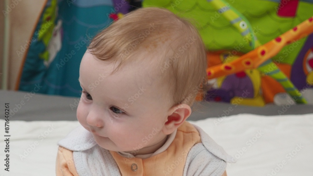Fototapeta premium Adorable happy blonde infant baby playing with kids toys at home while sitting on carpet floor in living room. Portrait of smiling cute child toddler using colorful toys, copy space