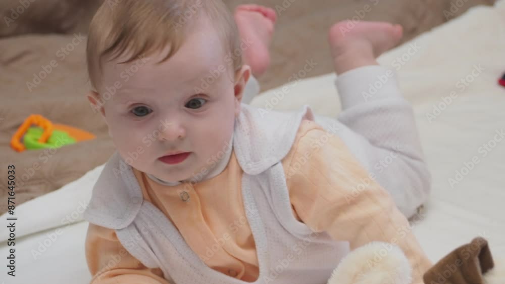 Adorable happy blonde infant baby playing with kids toys at home while sitting on carpet floor in living room. Portrait of smiling cute child toddler using colorful toys