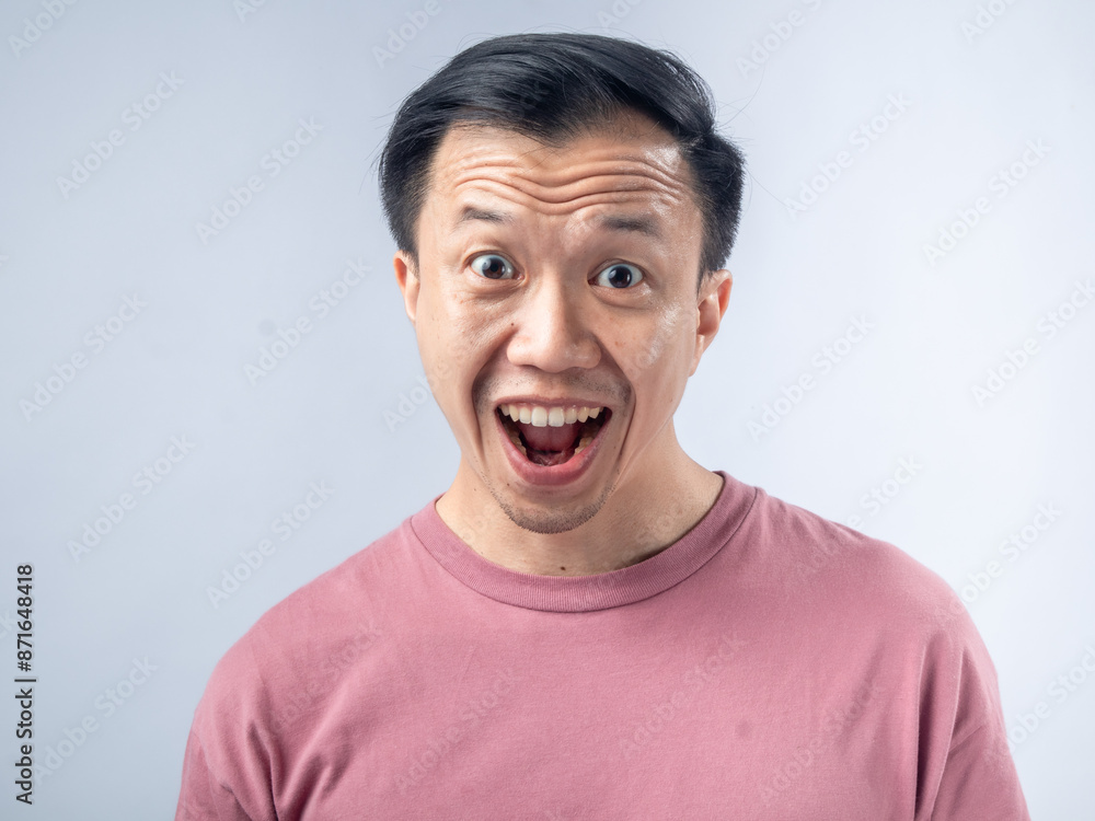A cheerful man in a pink shirt laughs heartily, his eyes closed and mouth wide open, exuding joy. The background is a plain, light blue backdrop, highlighting his vibrant expression A cheerful man in a pink shirt laughs heartily, his eyes closed and mouth wide open, exuding joy. The background is a plain, light blue backdrop, highlighting his vibrant expression