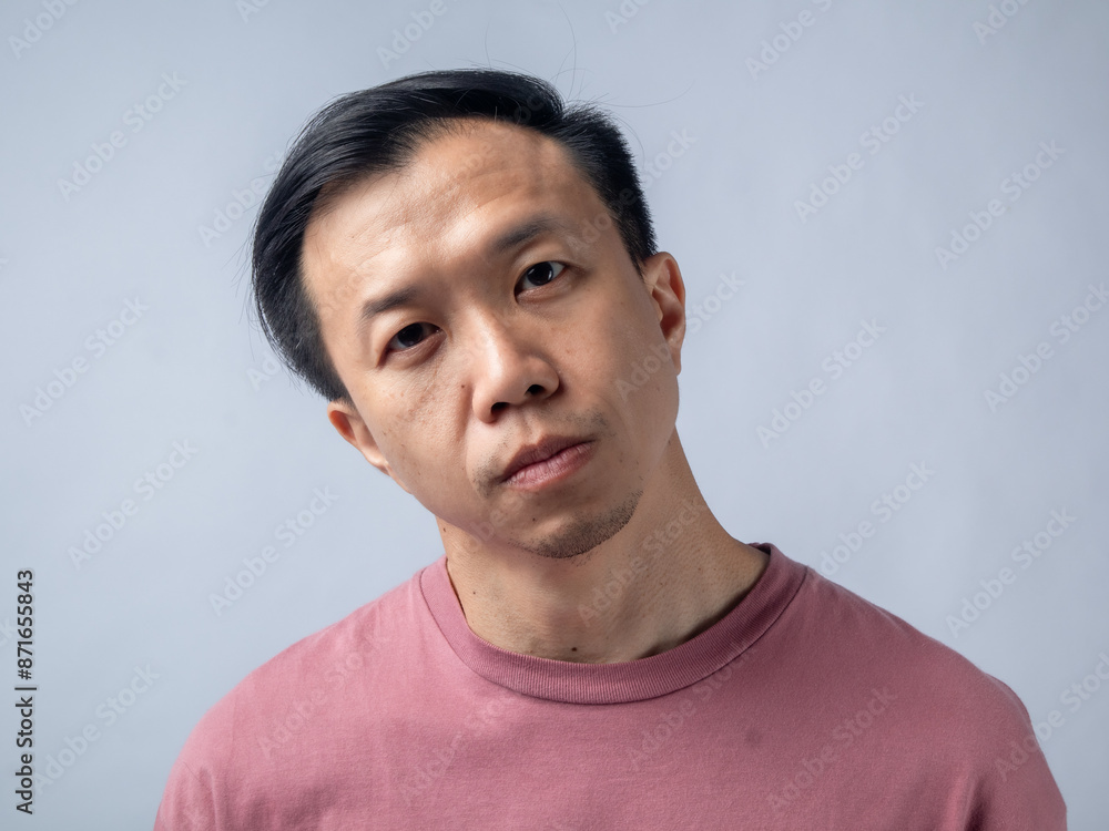 A serious man in a pink shirt gazes intensely at the camera, showing a stern expression. The plain light blue backdrop emphasizes his focused and contemplative demeanor.