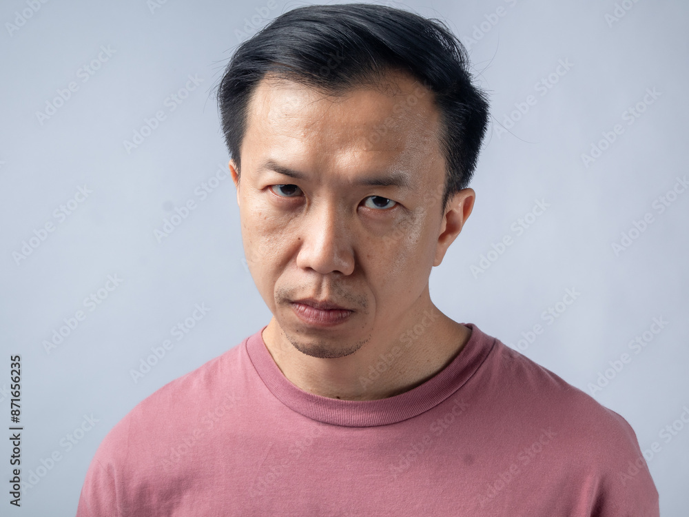 A serious man in a pink shirt gazes intensely at the camera, showing a stern expression. The plain light blue backdrop emphasizes his focused and contemplative demeanor. A serious man in a pink shirt gazes intensely at the camera, showing a stern expression. The plain light blue backdrop emphasizes his focused and contemplative demeanor.